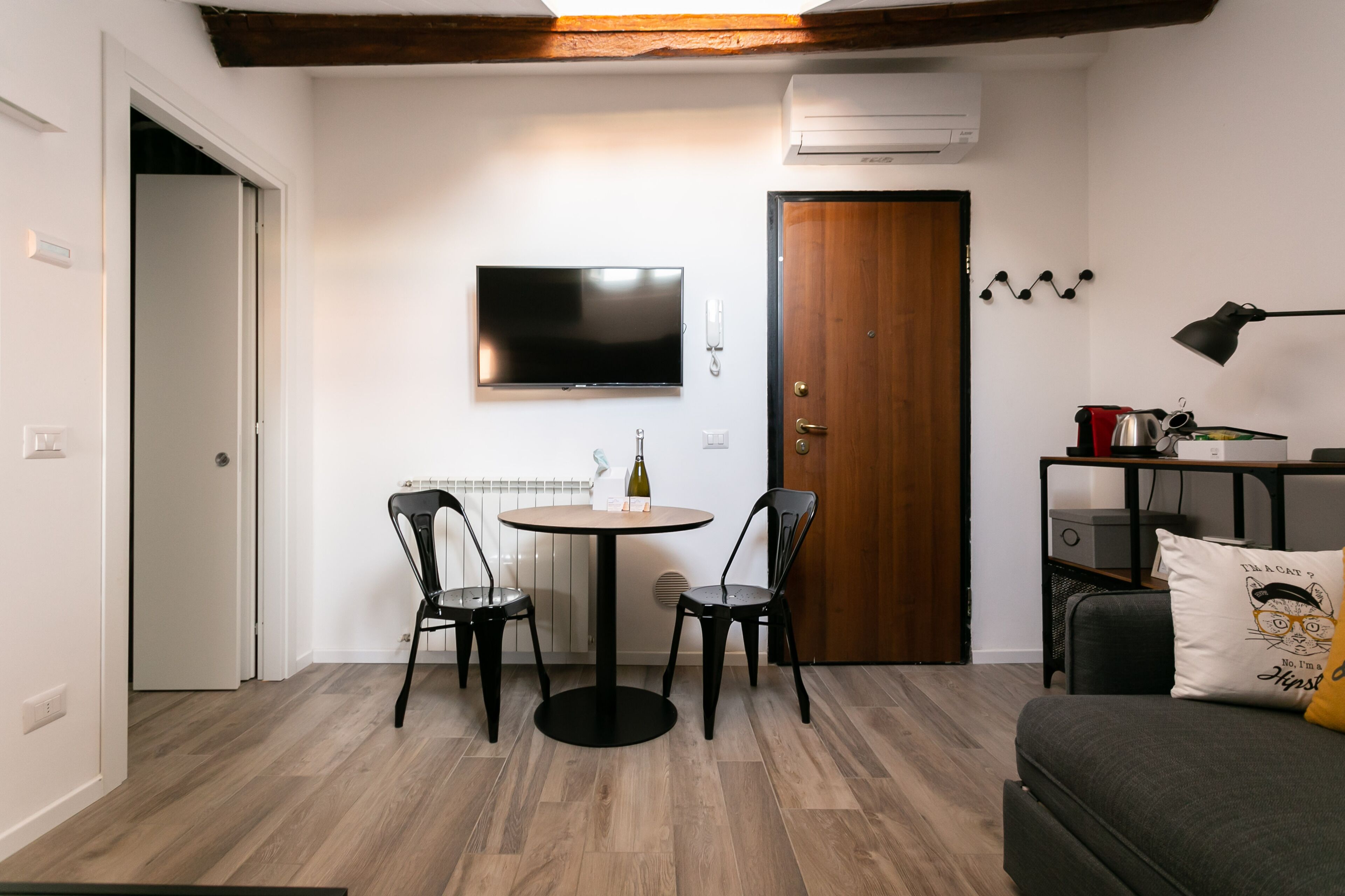 Un espace de vie compact comprenant un coin repas, un canapé, un téléviseur fixé au mur et une porte avec un porte-manteau.
