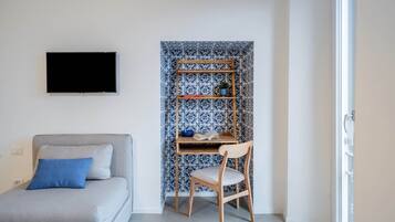 A room with a grey sofa, a wooden chair, a TV, and a bookshelf against a patterned wall.