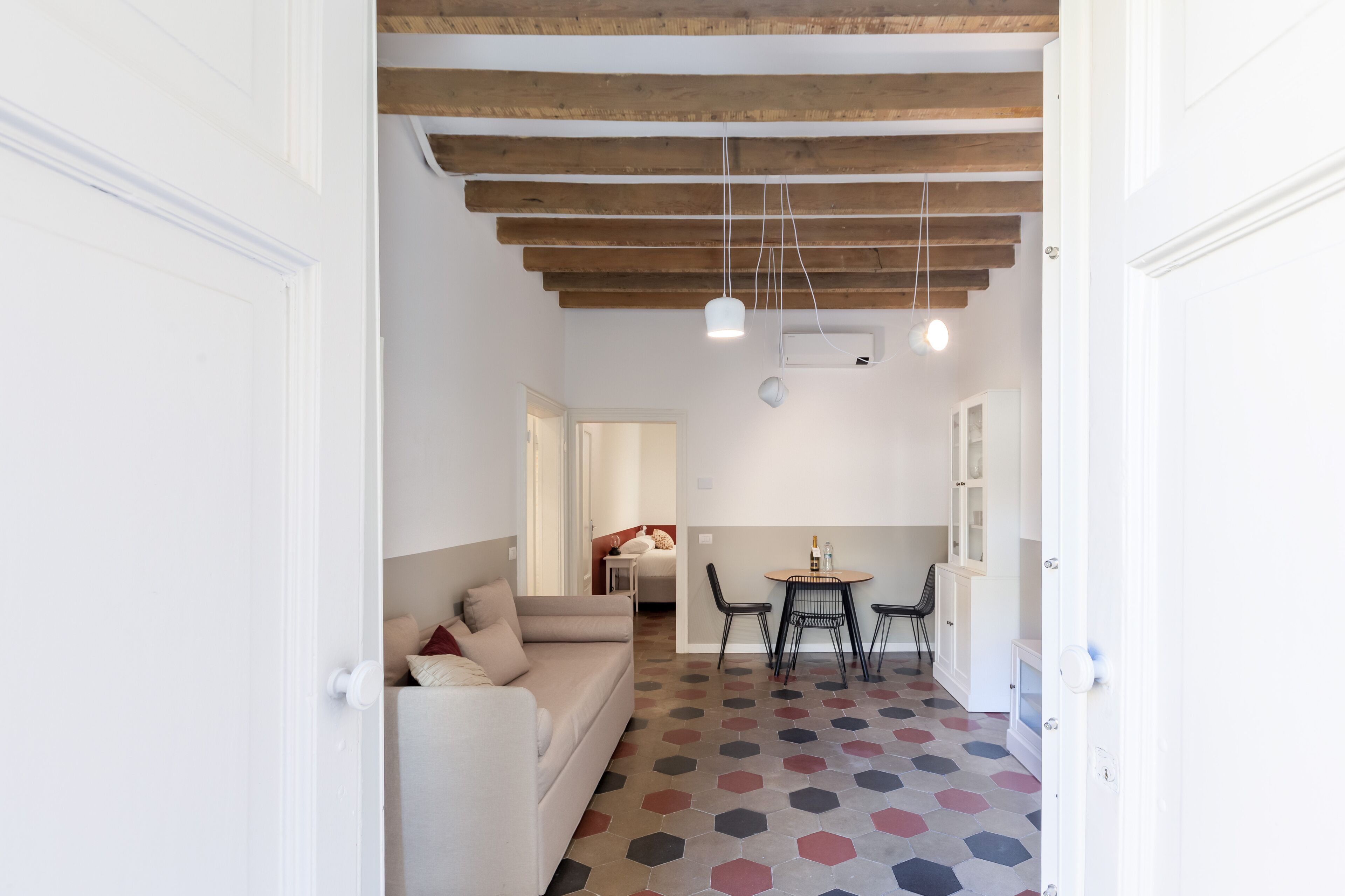 Un interior moderno con techo de madera, un sofá blanco, una mesa de comedor con sillas y un suelo estampado.