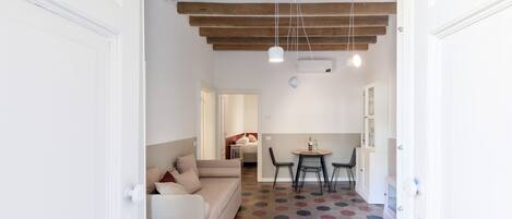 Un interior moderno con techo de madera, un sofá blanco, una mesa de comedor con sillas y un suelo estampado.
