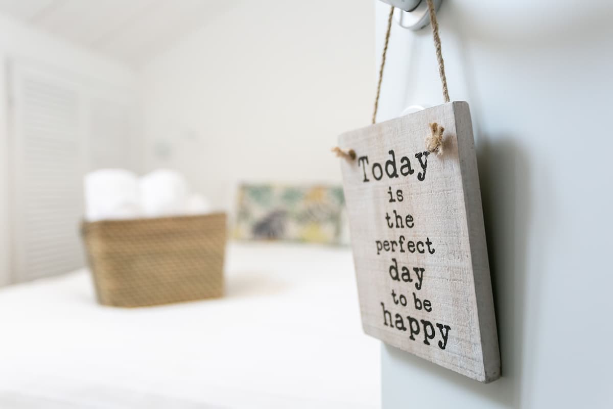 A wooden sign with the text "Today is the perfect day to be happy" hanging on a wall.