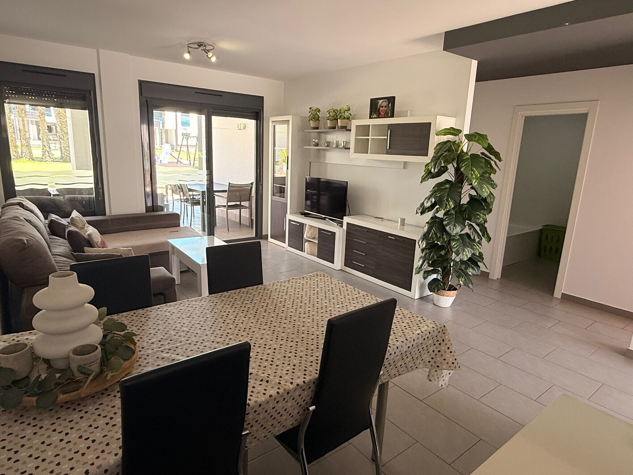 A modern living room with a dining table, chairs, a sofa, a TV, and a large plant.