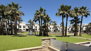 Un patio con mesa y sillas, rodeado de palmeras y un edificio de estilo arquitectónico moderno.