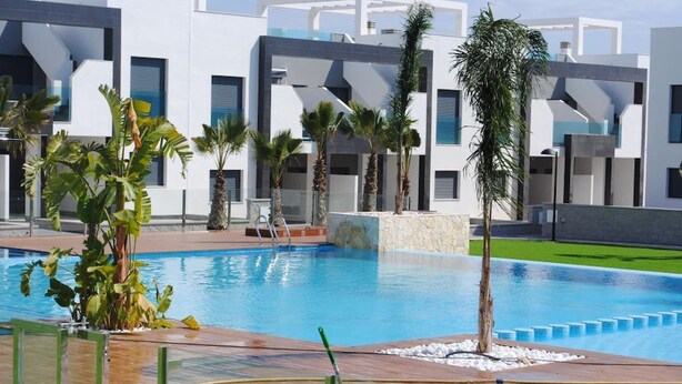 A modern pool area with a rectangular pool, surrounded by palm trees and a white building with large windows. - Penthouse Oasis beach IV La zenia (La Zenia)