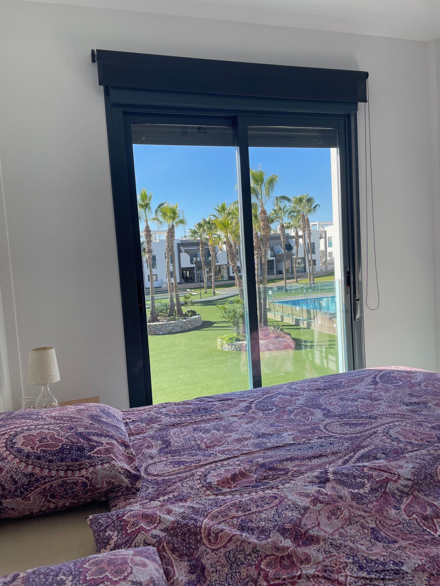 Une chambre d’hôtel avec un lit, une lampe et une vue sur une piscine et des palmiers.