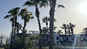 A landscaped area with palm trees, a stone wall, and a poolside area with a clear sky. - Penthouse Oasis beach II La zenia (La Zenia)