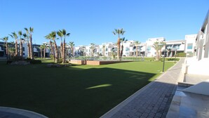 A modern hotel courtyard with artificial grass, palm trees, and a paved walkway. - Ground floor Oasis Beach II La Zenia (La Zenia)