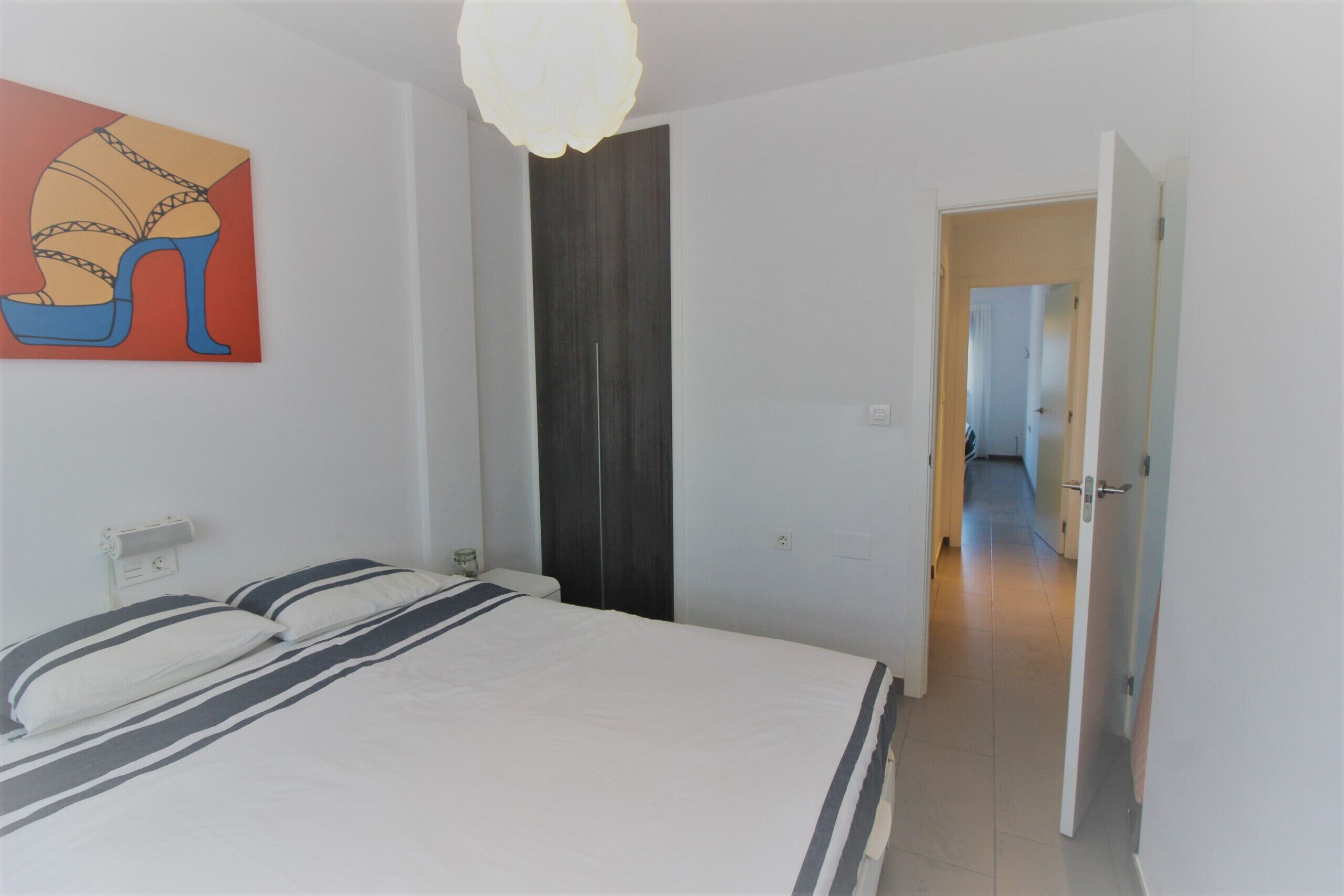 A bedroom with a bed, a painting, a wardrobe, and a hallway leading to another room.