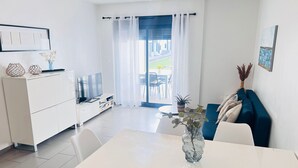 A modern, well-lit living area with a dining table, white sofa, and a TV on a white cabinet. - Ground floor Oasis Beach II La Zenia (La Zenia)