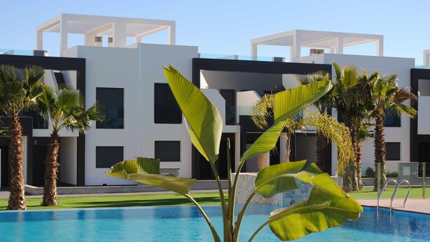 A modern pool area with a clear blue pool, surrounded by palm trees and a contemporary building with large windows and a white facade. - Ground floor Oasis Beach II La Zenia (La Zenia)
