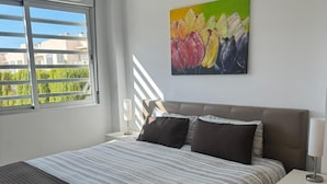 Une chambre à coucher moderne avec un grand lit, une table de chevet, un tableau et une fenêtre avec des stores.