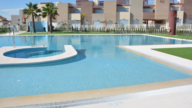 Une piscine à bord incurvé, entourée d’une clôture et de palmiers.