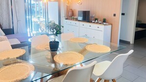 Un espace repas moderne avec une table en verre, des chaises blanches et des sets de table en fibres tressées.