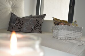 Un coin salon accueillant avec un canapé blanc, des coussins à motifs gris et un panier en osier rempli de magazines.