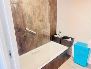 Une salle de bain avec une douche à parois de verre, une baignoire blanche et un panier à linge bleu.