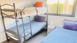Une chambre avec un lit superposé, dont le lit du bas est utilisé, un lit simple et une table de chevet avec une lampe.
