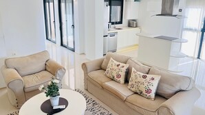 A modern living room with a beige sofa, a coffee table with a plant, and a kitchen area in the background.