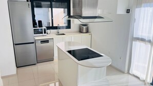 A modern kitchen with a stainless steel refrigerator, microwave, dishwasher, and a central island with an induction cooktop.