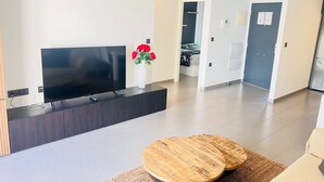 A modern living room with a flat-screen TV, a wooden coffee table, and a vase with red flowers.
