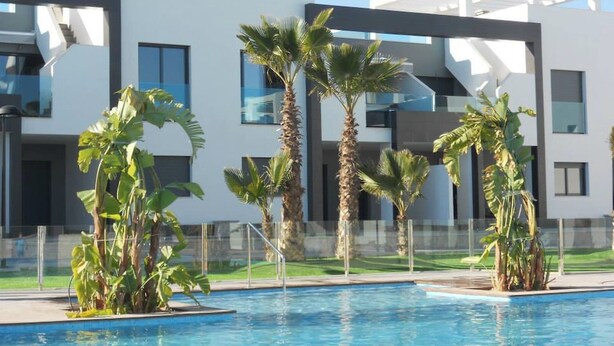 A modern building with a pool area, surrounded by palm trees and a clear blue sky.