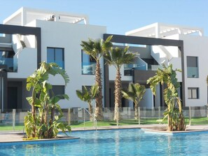 A modern building with a pool area, surrounded by palm trees and a clear blue sky. - Penthouse Oasis beach V La zenia (La Zenia)