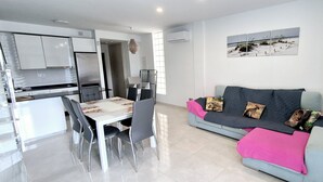 A modern kitchen with white cabinets and stainless steel appliances, a dining area with a white table and chairs, and a grey sofa with animal-themed cushions. - Duplex private pool Sinergia Los Alcazares (Los Alcazares)