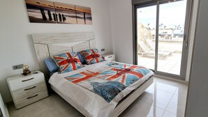 A bedroom with a large bed, a nightstand, a drawer unit, and a view of the outside through a sliding glass door. - Duplex private pool Sinergia Los Alcazares (Los Alcazares)