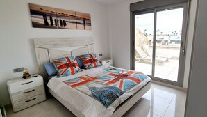 A bedroom with a large bed, a nightstand, a window with a view of the beach, and a painting above the bed. - Duplex private pool Sinergia Los Alcazares (Los Alcazares)