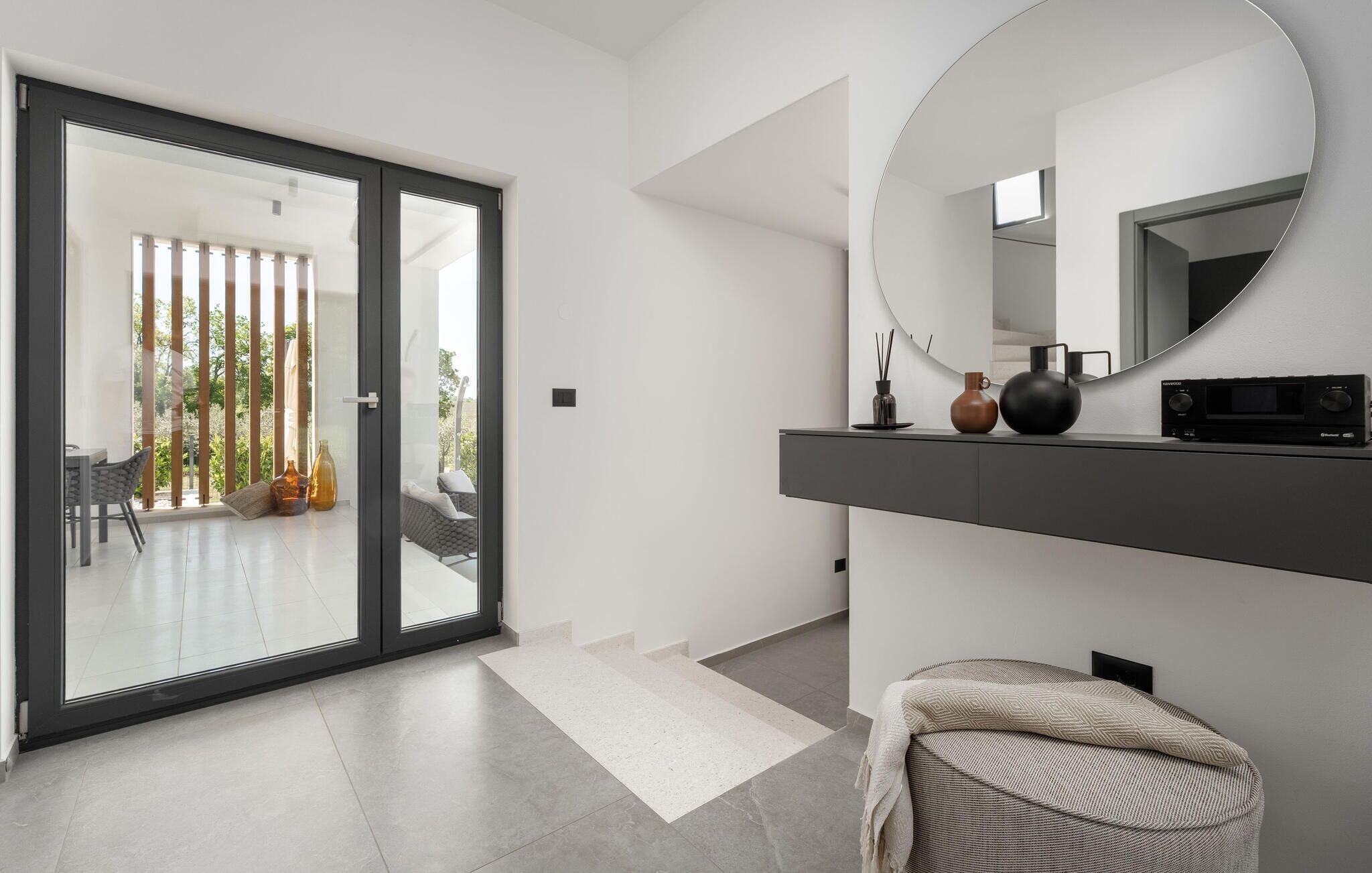 Un intérieur moderne avec une porte-fenêtre coulissante donnant sur un balcon, un miroir rond et une console au design minimaliste.