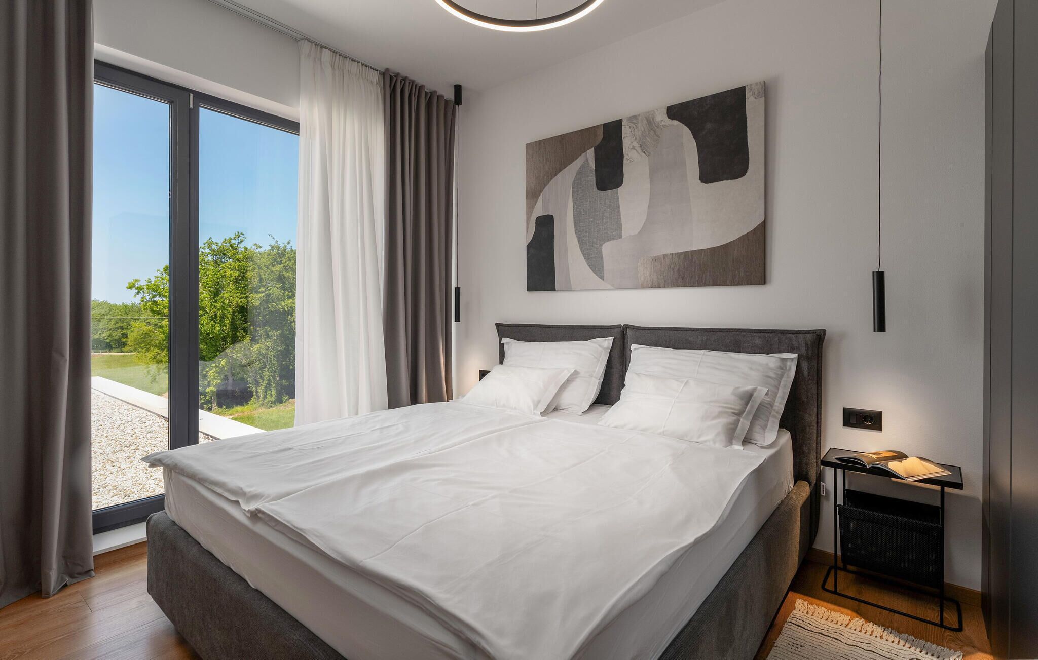 Une chambre moderne avec un grand lit, une vue sur la verdure et une peinture abstraite contemporaine accrochée au mur.