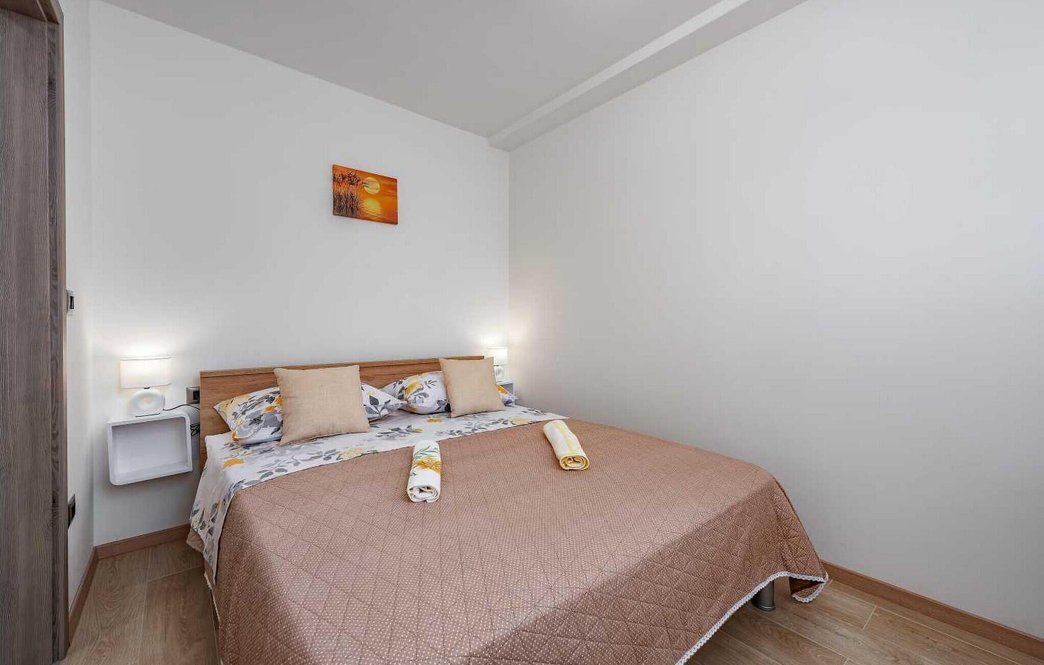 Een net opgemaakt bed met een bruine spreidek, twee bedlampjes en een aan de muur hangend kunstwerk.