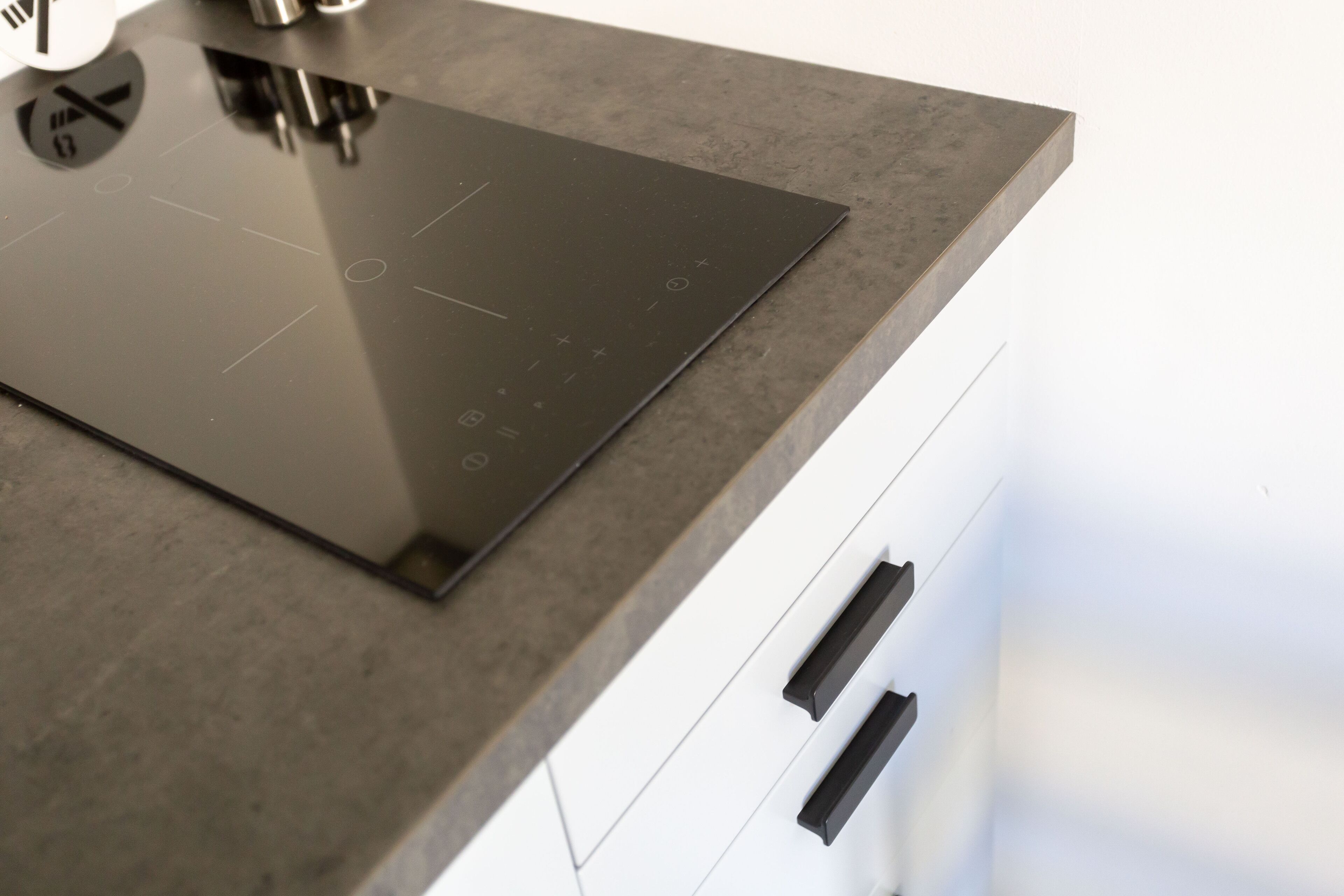 A kitchen with a modern induction cooktop and a white cabinet with black handles.