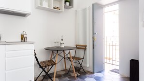 Una cocina compacta con muebles blancos, una mesa de comedor con dos sillas y un radiador.