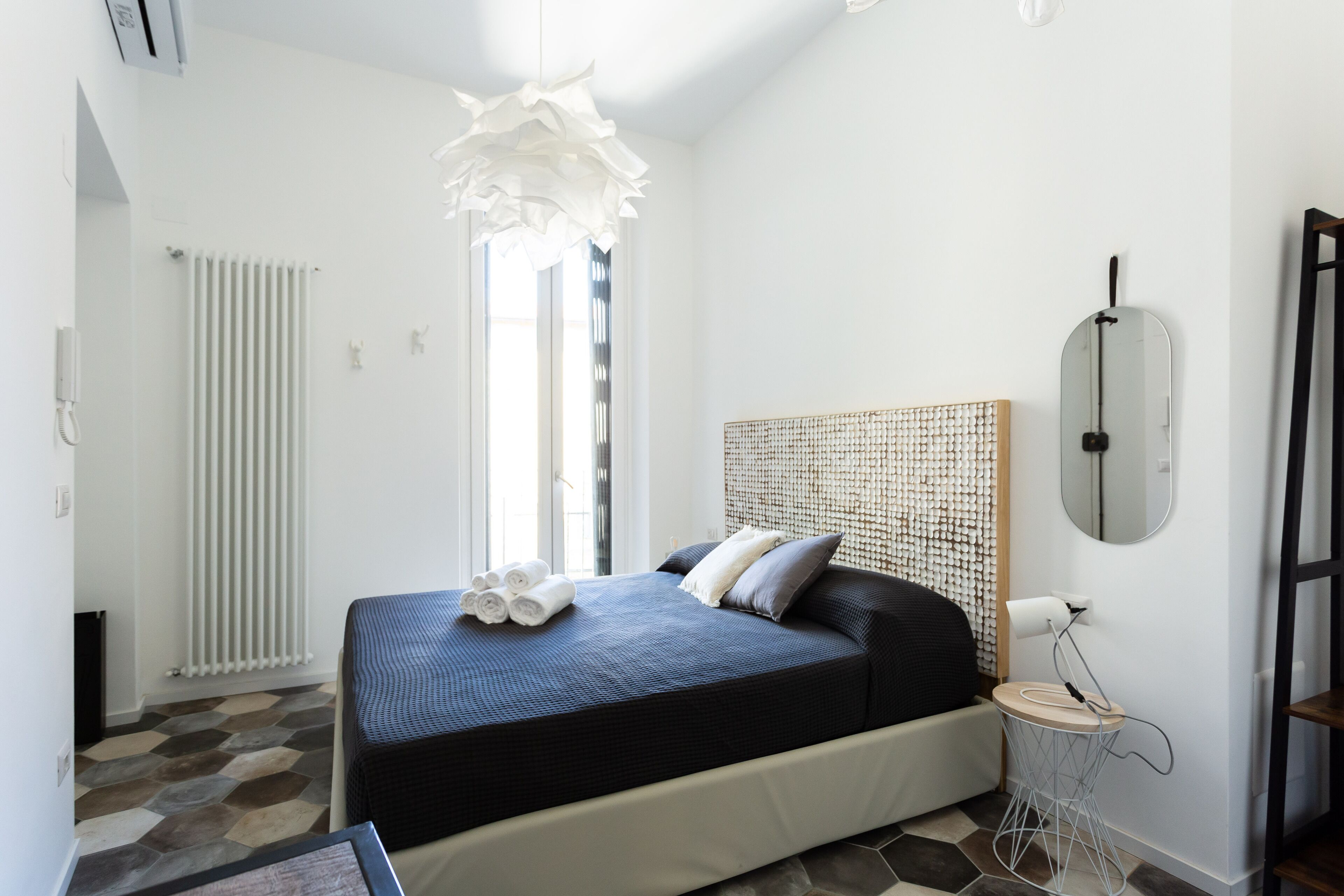 A modern bedroom with a large bed, a bedside table, a mirror, and a radiator.