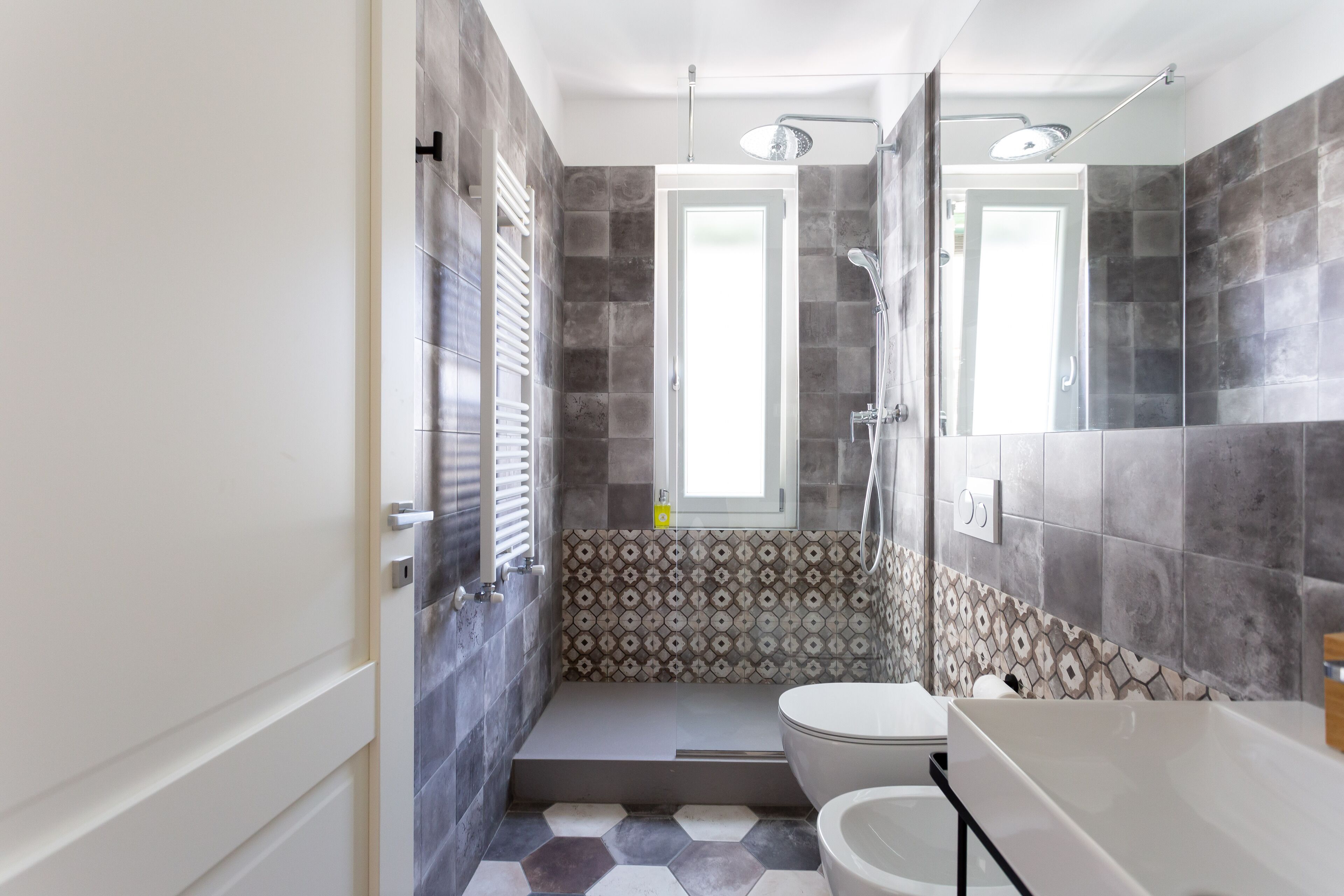 A modern bathroom with a shower, toilet, and sink, featuring patterned tiles and a window.