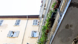 Un edificio con varias ventanas, algunas con contraventanas, y balcones adornados con plantas en macetas.