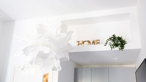 Un interior moderno con techo blanco, un candelabro decorativo también blanco y un letrero que dice 'HOME' sobre una planta.