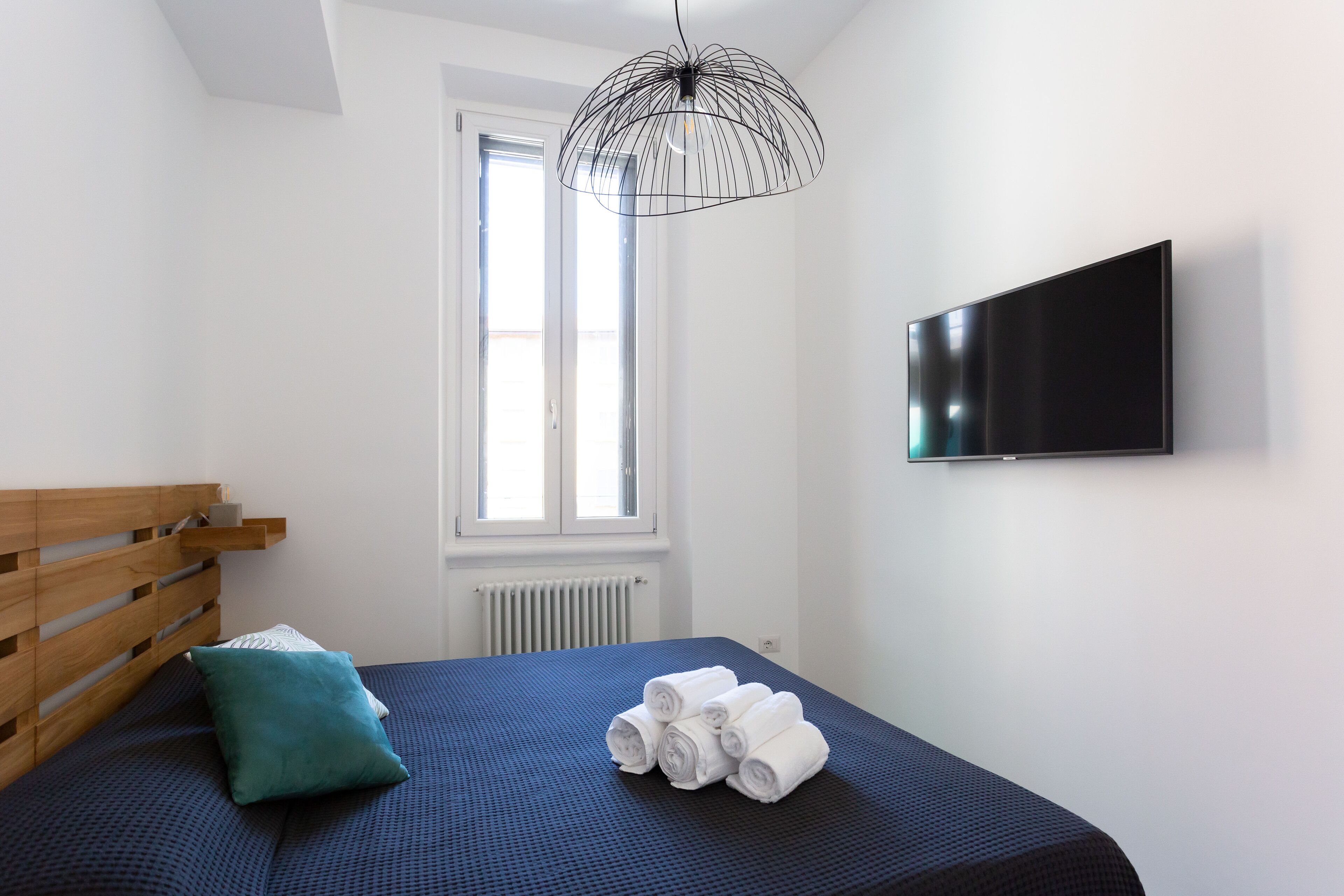 A bedroom with a bed, a TV, a window, and a radiator.