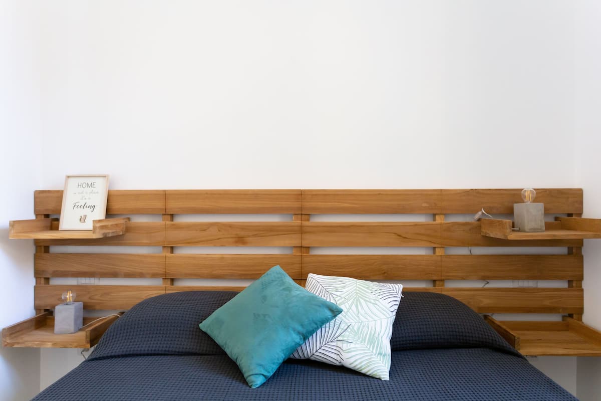A bed with a wooden headboard, two pillows, and a small framed sign on a shelf.