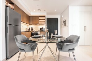 A modern kitchen with a built-in refrigerator, wooden cabinets, and a glass dining table with two chairs. - Stayis - 1 BR Iconic Burj Khalifa View (Dubai)