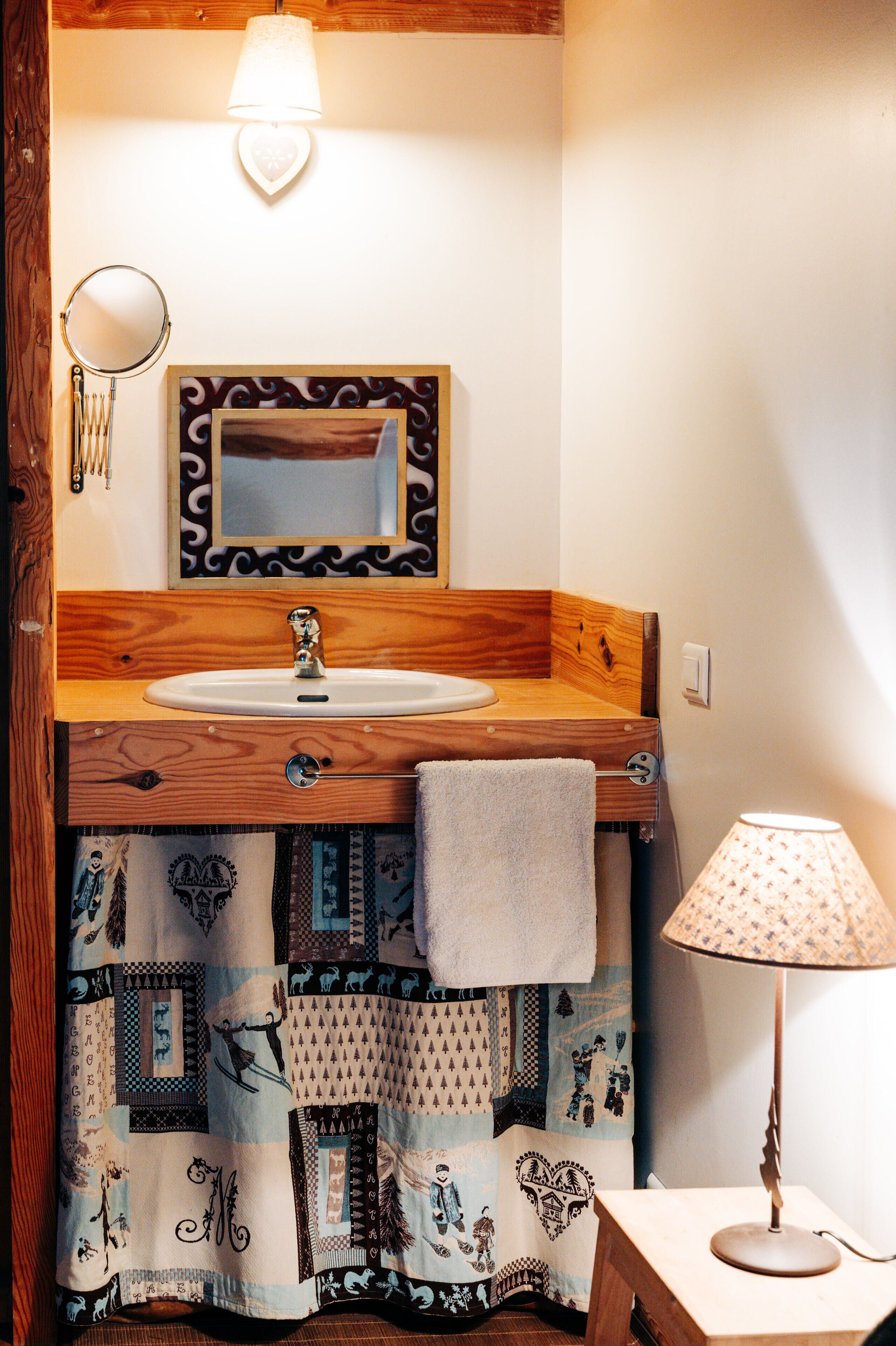 A bathroom with a wooden vanity, a sink, a mirror, a towel, and a lamp.