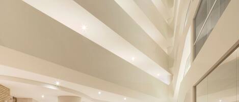A spacious lobby with a curved yellow sofa, a reception desk, and a staircase leading to upper floors.