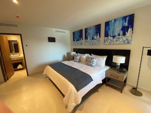 Quarto moderno com uma cama grande, mesas de cabeceira, um criado-mudo, abajur e obras de arte na parede.