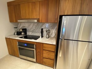 Una cocina moderna con armarios de madera, un refrigerador de acero inoxidable, un horno empotrado, una cafetera y un bloque para cuchillos.