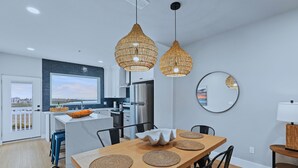 A modern kitchen with white cabinets, a large island, and a dining area with a wooden table and chairs. - Experience coastal luxury at Sunny Isle Sanctuary. This chic 2BR/2BA features a designer kitchen, private bay-view balcony, and modern finishes. Reliable service meets the comfort of home. Perfect for your high-end SPI getaway. Book your stay now! (South Padre Island)