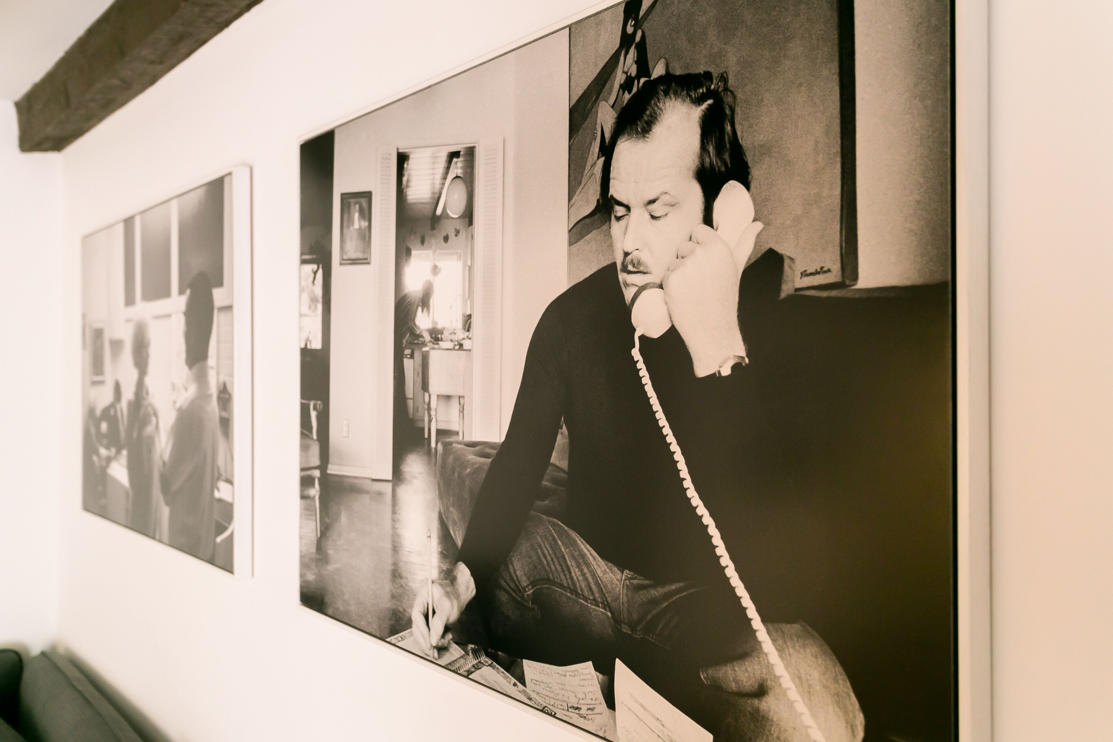 A wall with framed photographs and a painting of a person on a telephone.
