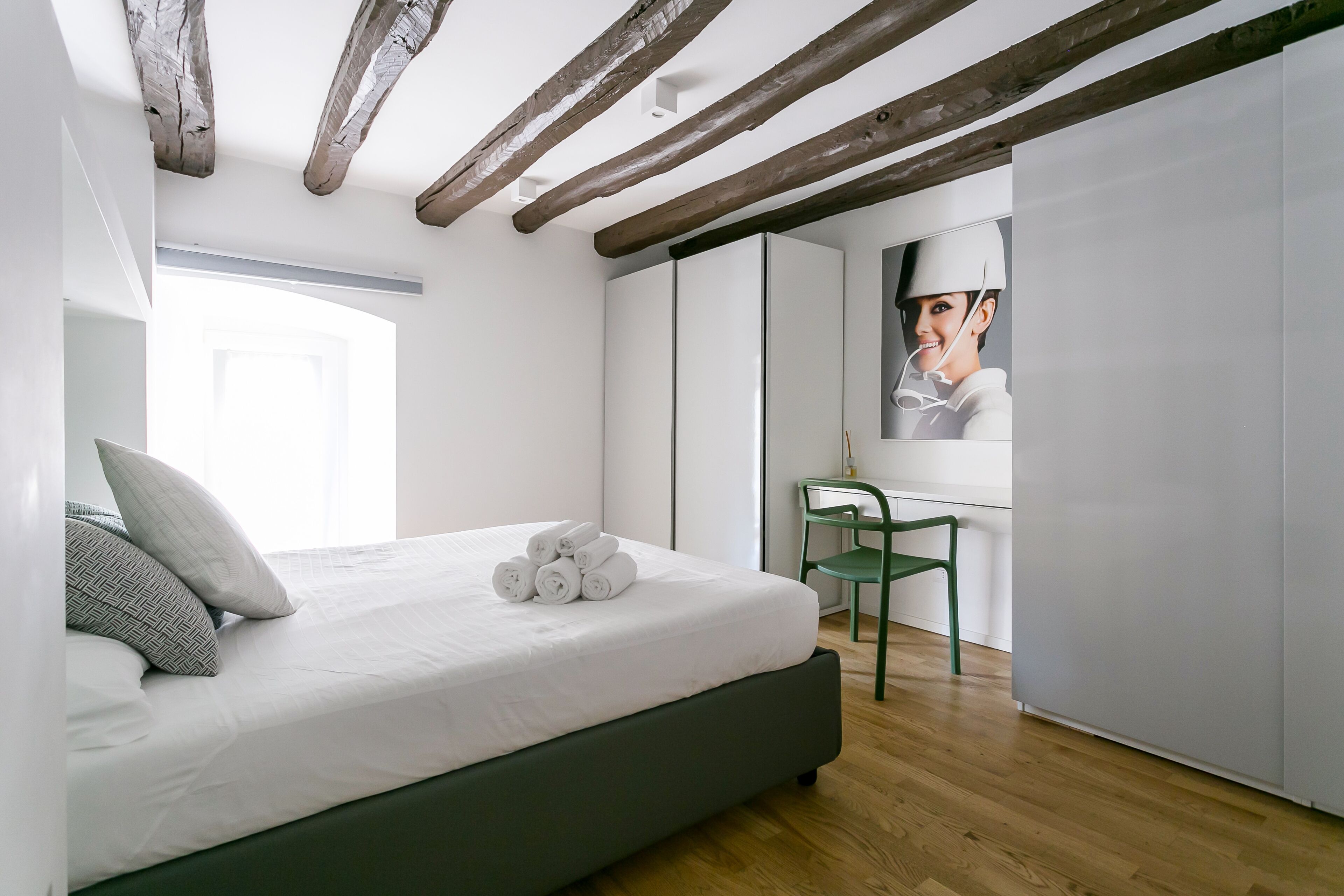 Un dormitorio moderno con una cama grande, un sillón verde y un televisor montado en la pared.