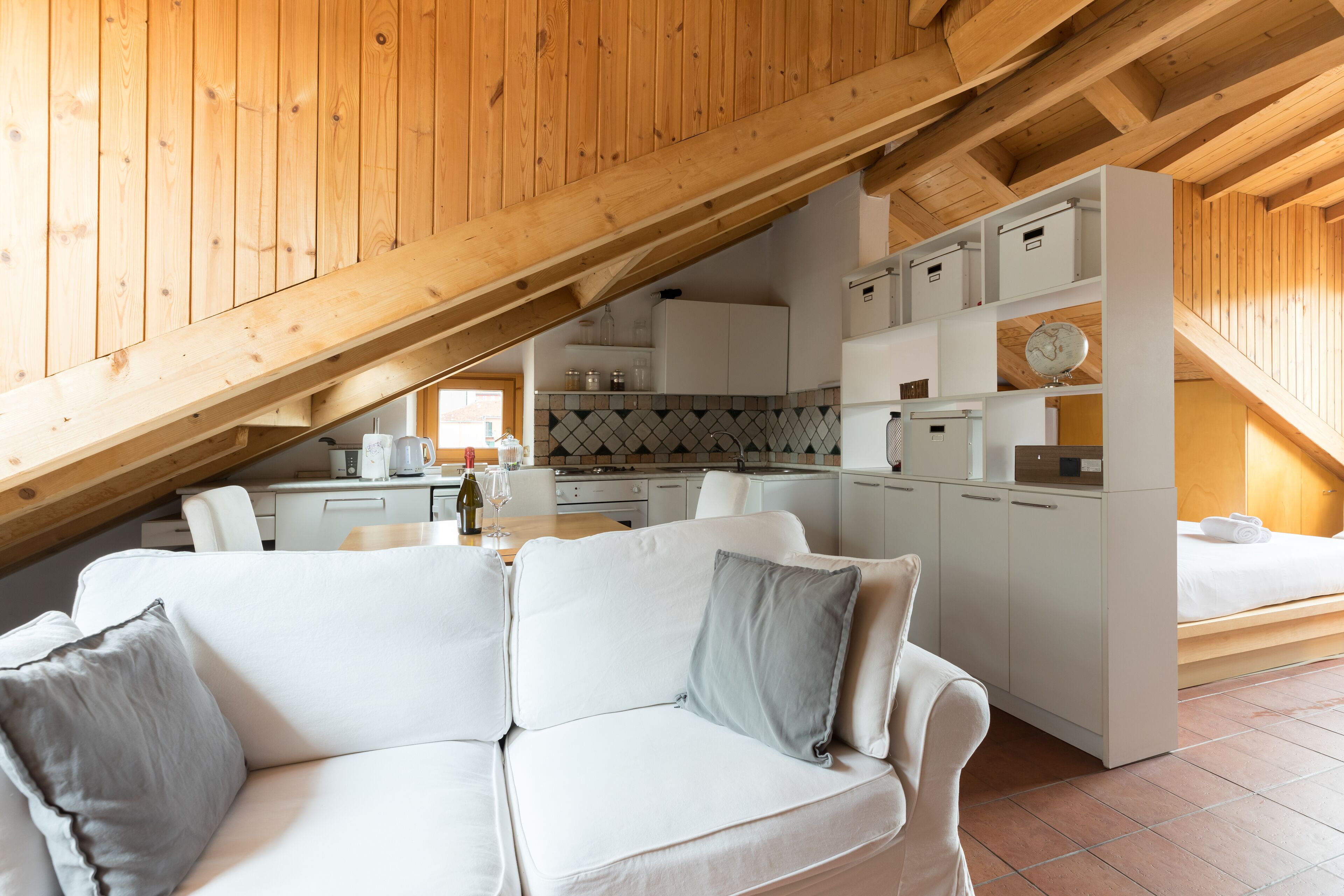 Une pièce confortable de style loft, avec un canapé blanc, une table à manger et un coin cuisine situé sous un plafond en bois incliné.