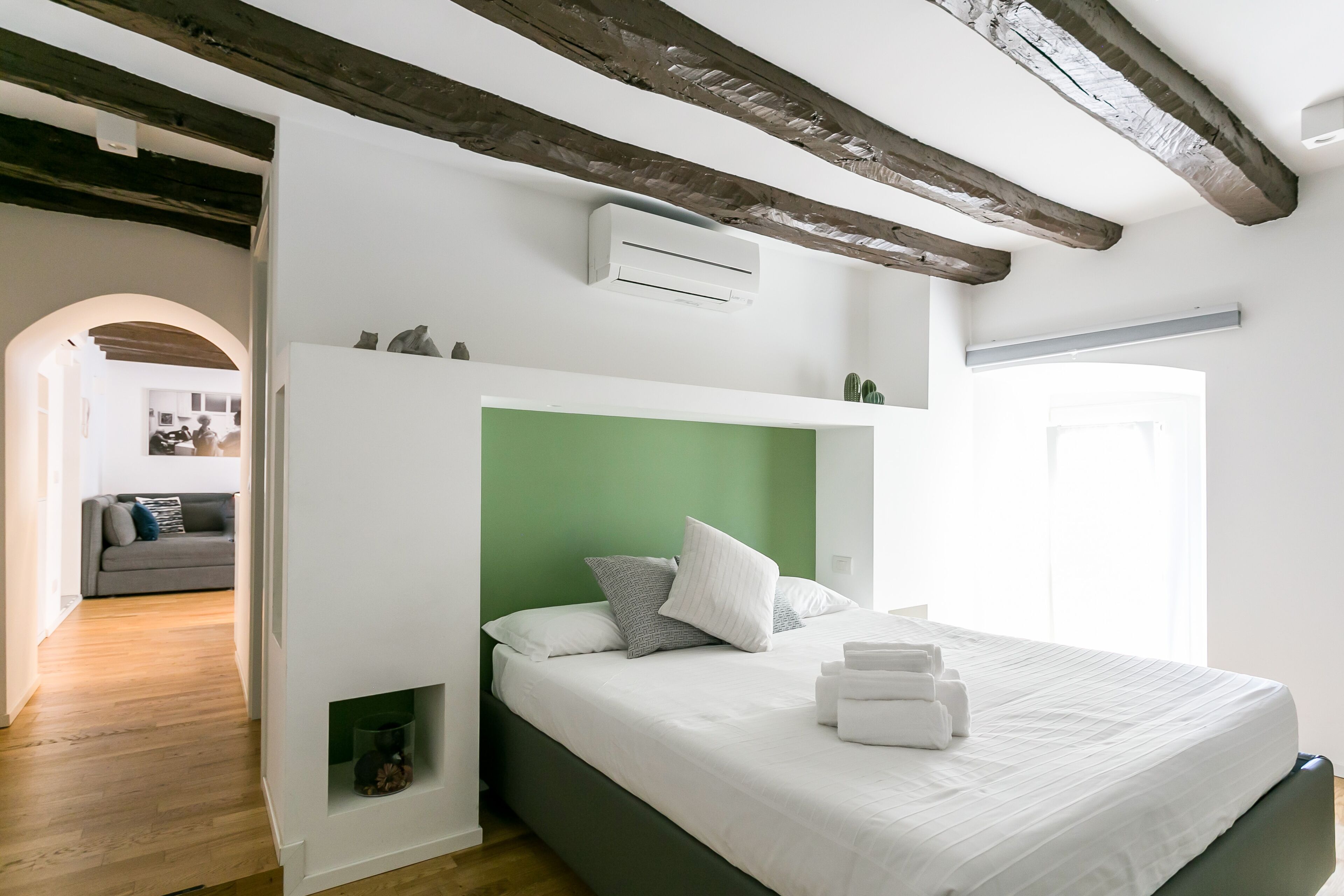 A bedroom with a green headboard, white bedding, and a built-in shelf with decorative items.