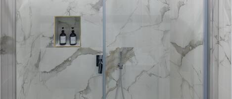 A glass-enclosed shower with marble walls and a tiled floor.